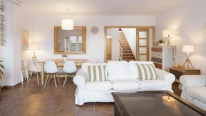 Ein Wohnzimmer mit weißem Sofa, einem Esstisch mit Stühlen, einer Treppe und einem großen Spiegel.