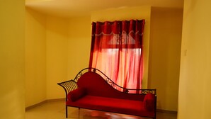A red sofa in a corner with a red curtain and a yellow wall. - Sakthi Hotel (Pollachi)