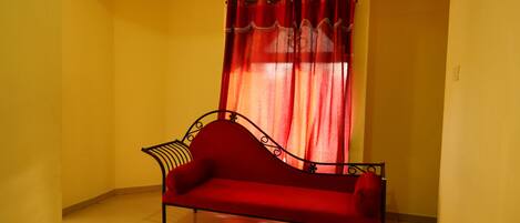 Um sofá vermelho num canto, com uma cortina vermelha e uma parede amarela.