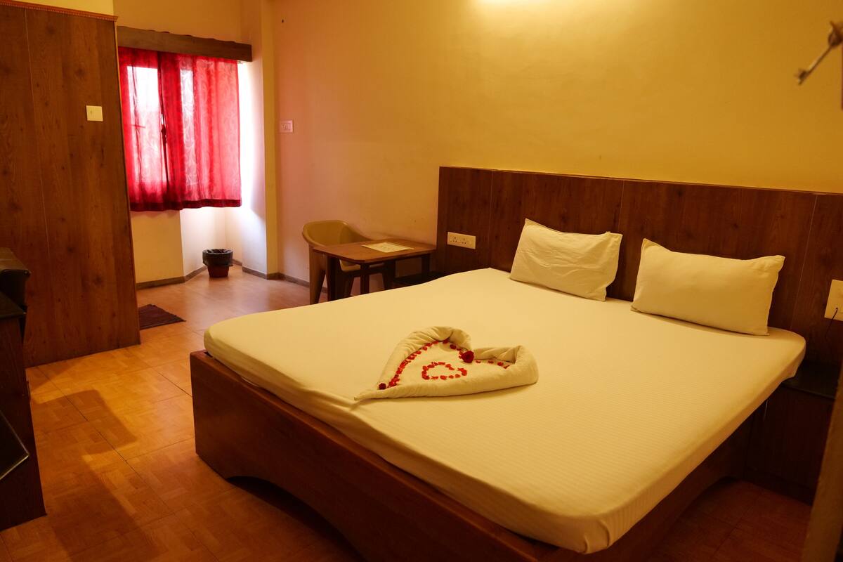A neatly made bed with white linens and a heart-shaped decoration, a wooden headboard, and a small wooden table with a chair.