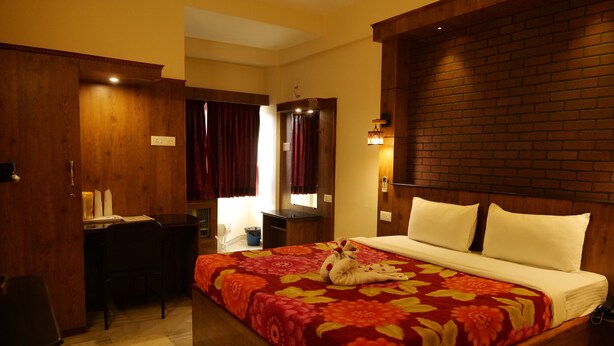 A hotel room with a wooden bed, a desk, and a chair. - Sakthi Hotel (Pollachi)