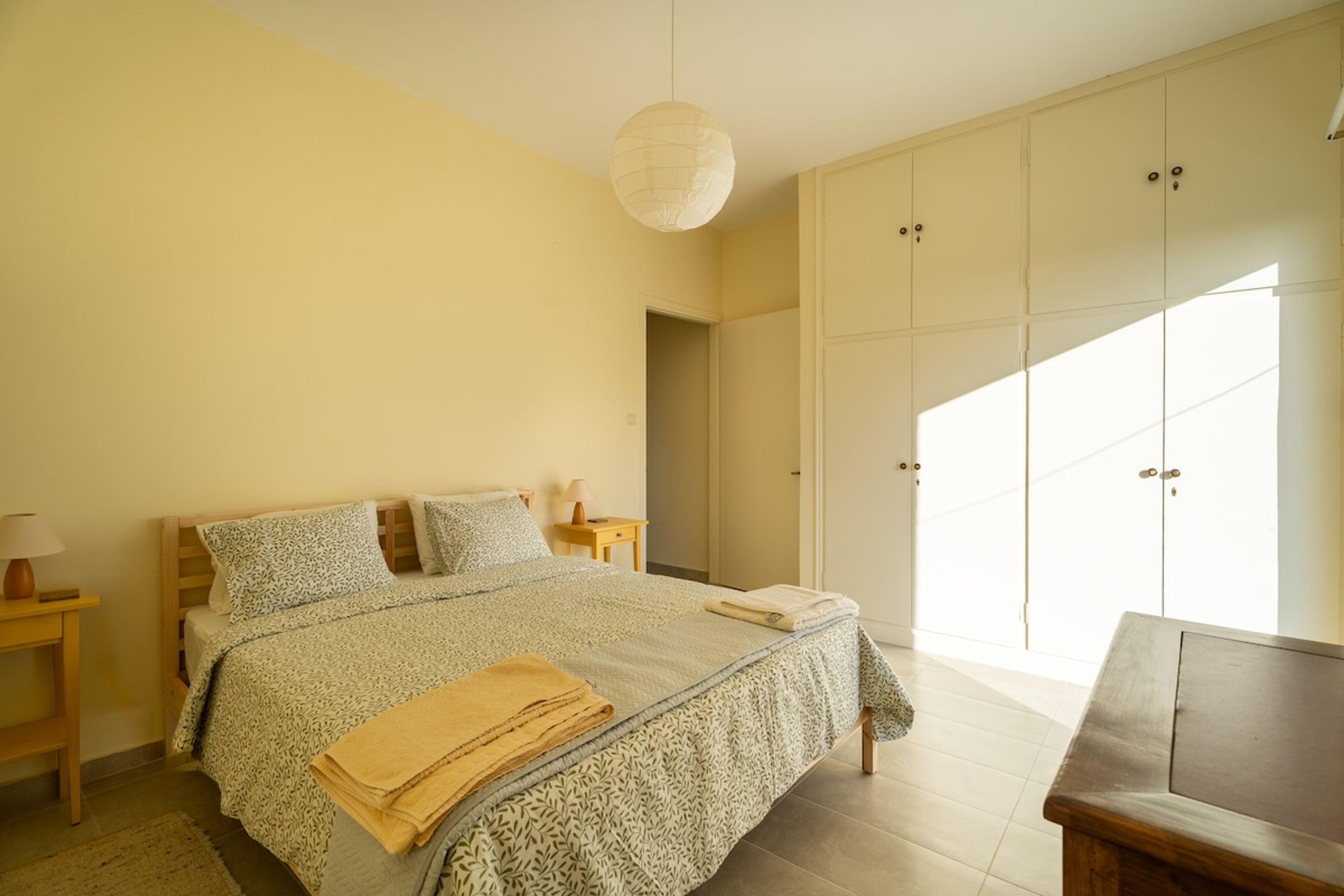 Une chambre à coucher comprenant un lit, des tables de chevet, une armoire et une grande fenêtre.
