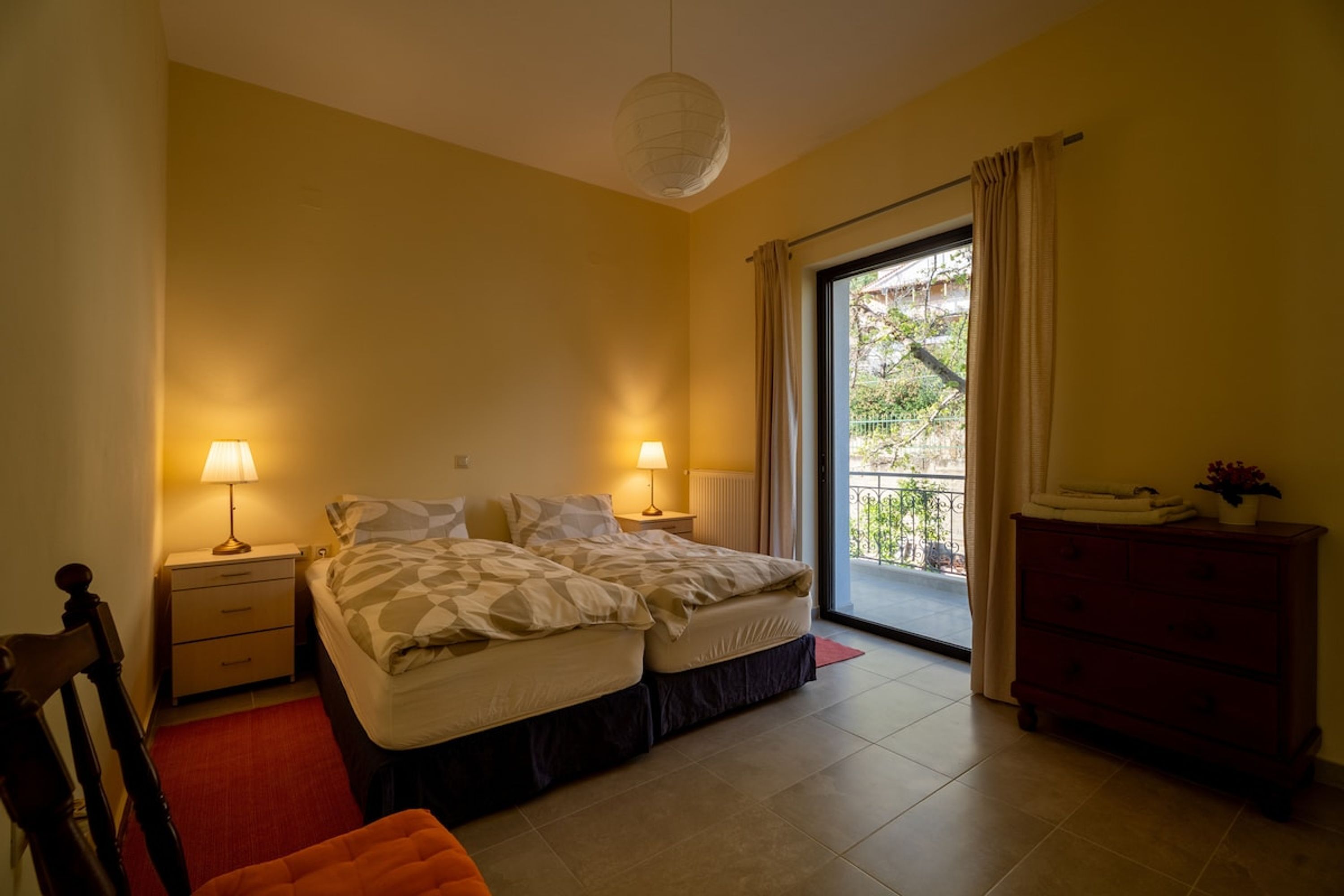 A bedroom with a bed, two bedside tables with lamps, a dresser, and a view of the outside balcony.