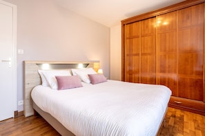 A bedroom with a bed, wooden wardrobe, and a nightstand with a lamp.