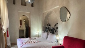 A bedroom with a bed, a red chair, a mirror, and two wall-mounted lamps. - Riad Bab Yacout (Marrakech)