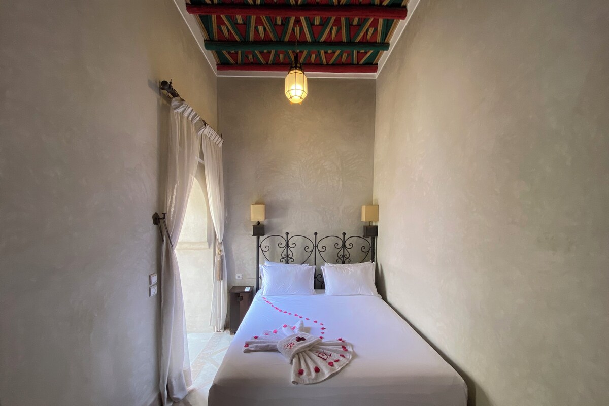 A bedroom with a bed, two bedside lamps, a ceiling with a patterned design, and a window with curtains.