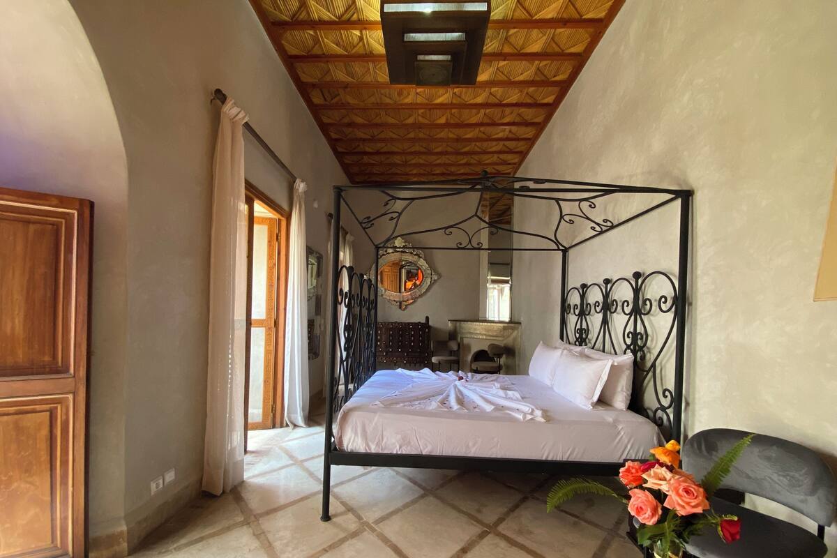 A bedroom with a four-poster bed, a wooden door, a mirror, and a vase with flowers.