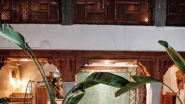 A poolside dining area with a table set for two, surrounded by potted plants and a view of a pool. - Riad Bab Yacout (Marrakech)
