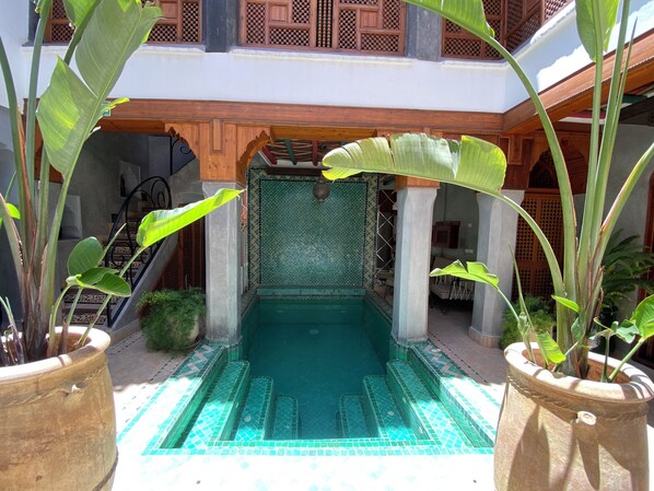 A pool area with tiled steps leading into a pool, surrounded by potted plants and wooden structures. - Riad Bab Yacout (Marrakech)