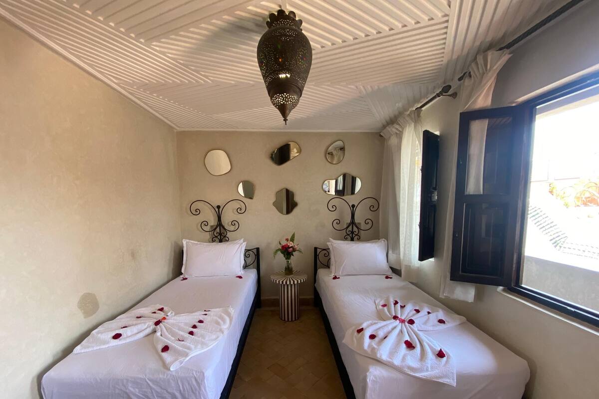 A room with two beds, a ceiling fan, a window with curtains, and a decorative mirror on the wall.