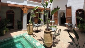 A courtyard with a tiled pool, potted plants, and outdoor seating. - Riad Bab Yacout (Marrakech)