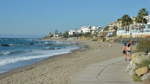 A beach with a concrete walkway, ocean waves, and buildings in the background.