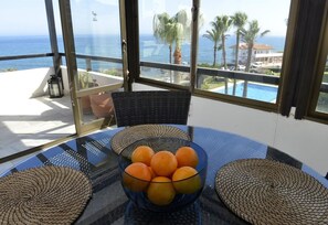 A glass table with a bowl of oranges, wicker chairs, and a view of the sea and palm trees. - Holiday Home 'Beachside Penthouse' with Sea View, Wi-Fi and Air Conditioning (La Cala de Mijas)