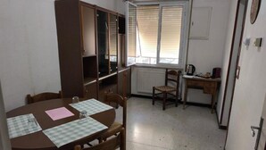 Une pièce de taille modeste comprenant une table à manger, des chaises, un petit coin cuisine et une fenêtre avec des stores.