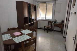 A compact room with a dining table, chairs, a small kitchen area, and a window with blinds. - Casa Fannì: Space, Comfort and Breathtaking Views (Varazze)
