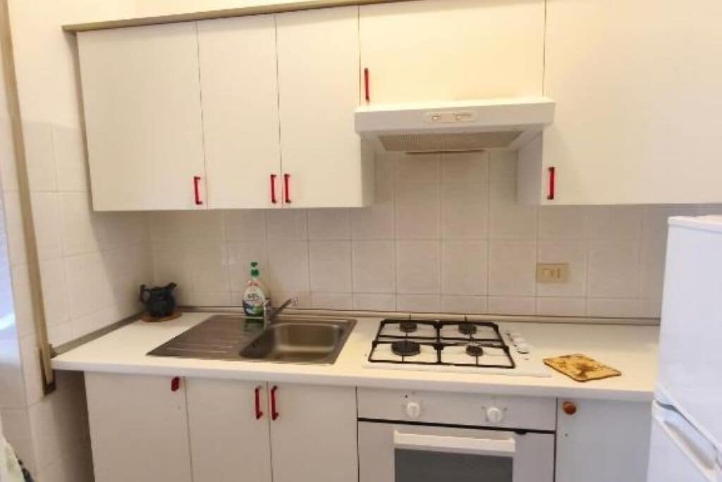 Une cuisine avec des meubles blancs, une cuisinière à gaz, un évier et un four à micro-ondes.