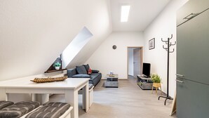 A modern loft-style living space with a dining area, a sofa, a television, and a coat rack. - Apartment 'Weitblick' (Top Floor Center) with Free Wi-Fi (max. 6 guests) (Pottenstein)