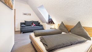 A bedroom with a sloped ceiling, a bed with pillows, a sofa, and a small table. - Apartment 'Weitblick' (Top Floor Center) with Free Wi-Fi (max. 6 guests) (Pottenstein)