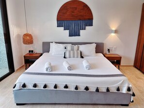 A neatly made bed with pillows and rolled towels, a wall-mounted light fixture, and a wooden headboard.