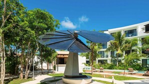 A modern building with a pool, surrounded by palm trees and a solar panel sculpture. - Studio with King Bed in La Veleta (Tulum)