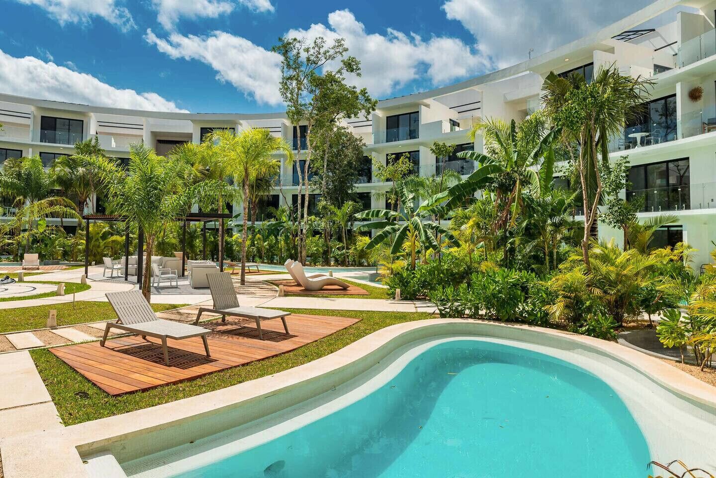 A modern hotel with a swimming pool, lounge chairs, and tropical landscaping.
