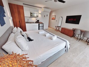 A modern hotel room with a large bed, a kitchenette, a flat-screen TV, and a seating area. - Studio with King Bed in La Veleta (Tulum)