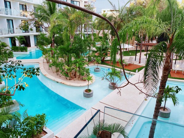 A pool area with multiple levels of balconies, surrounded by lush greenery and palm trees.