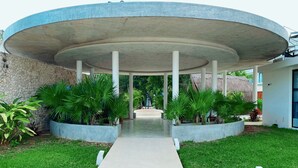 A modern building with a circular central structure, surrounded by a paved walkway and green landscaping. - Studio with King Bed in La Veleta (Tulum)