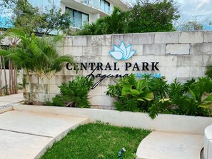 A sign for Central Park with a logo, surrounded by greenery and a stone wall.