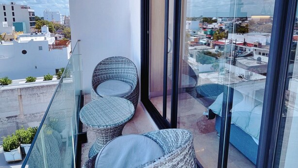 A balcony with wicker chairs, a glass door, and a view of the cityscape. - Centric Studio in 4th Floor with Balcony (Playa del Carmen)