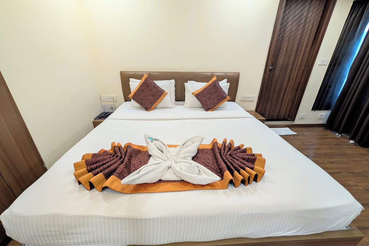 A hotel room with a neatly made bed, a wooden headboard, and a large window with curtains.