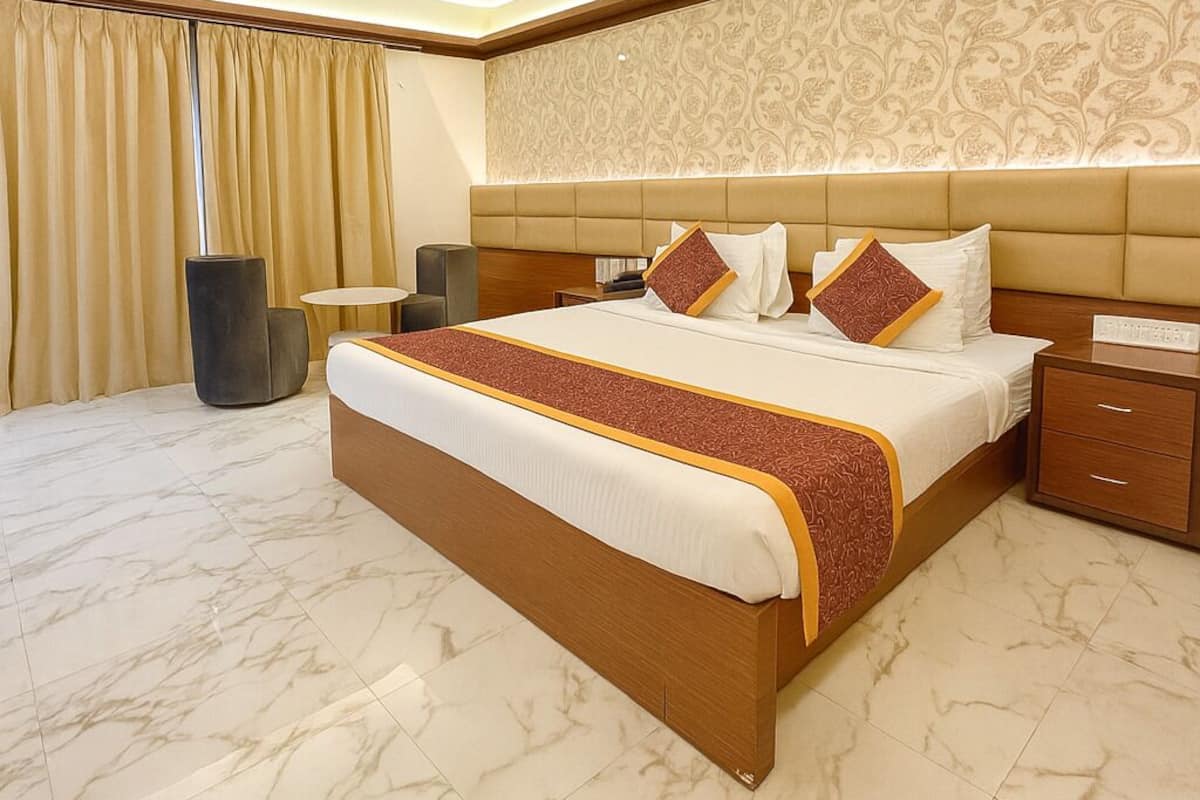A spacious bedroom with a large bed, a nightstand, a chair, and a patterned wall.