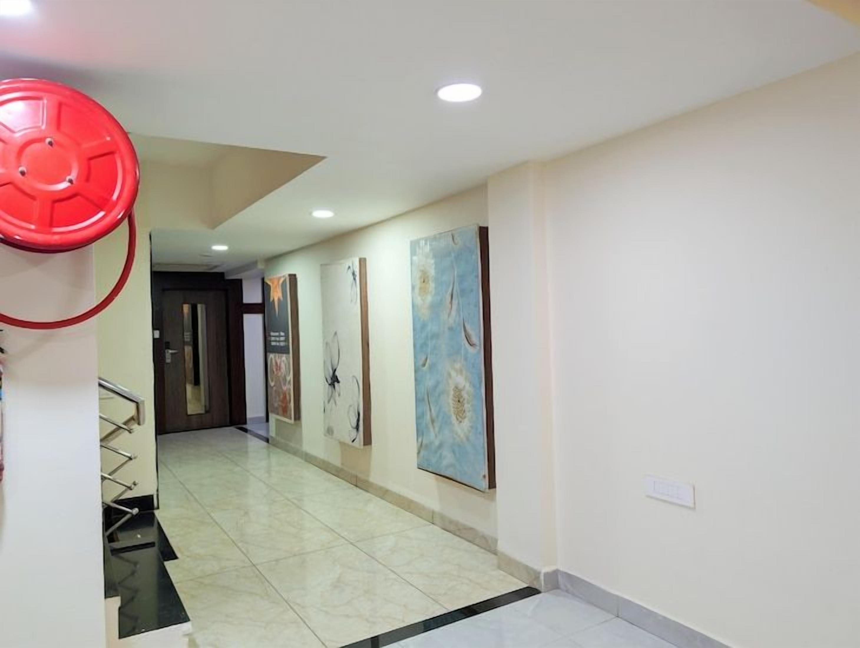 A hotel hallway with artwork on the walls, a red fire alarm, and a staircase.