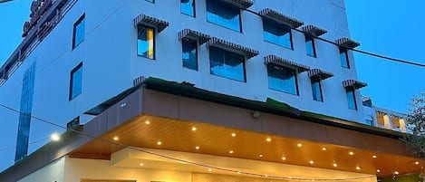 A multi-story hotel with a modern design, featuring a prominent entrance with a well-lit facade and a signboard.