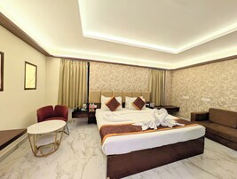A hotel room with a large bed, a small round table, a sofa, and a mirror.
