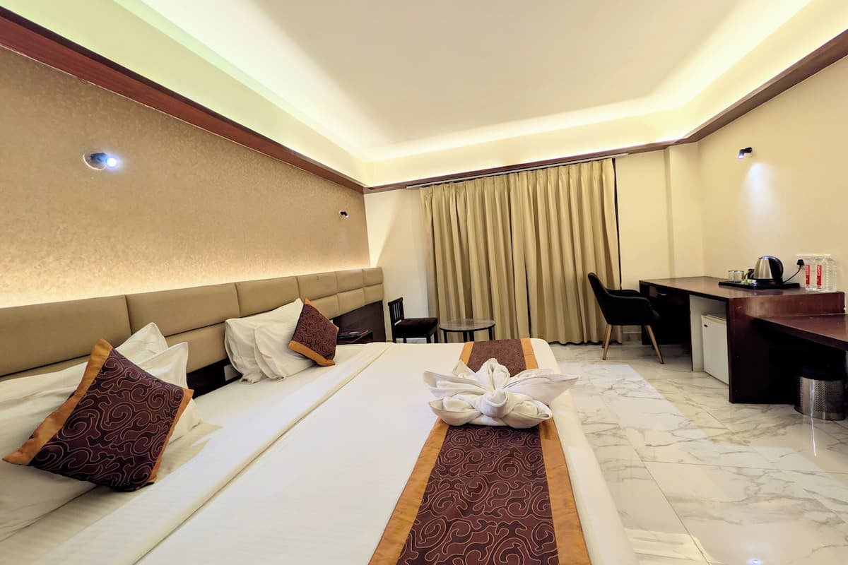 A hotel room with a large bed, a desk, a chair, and a small refrigerator.