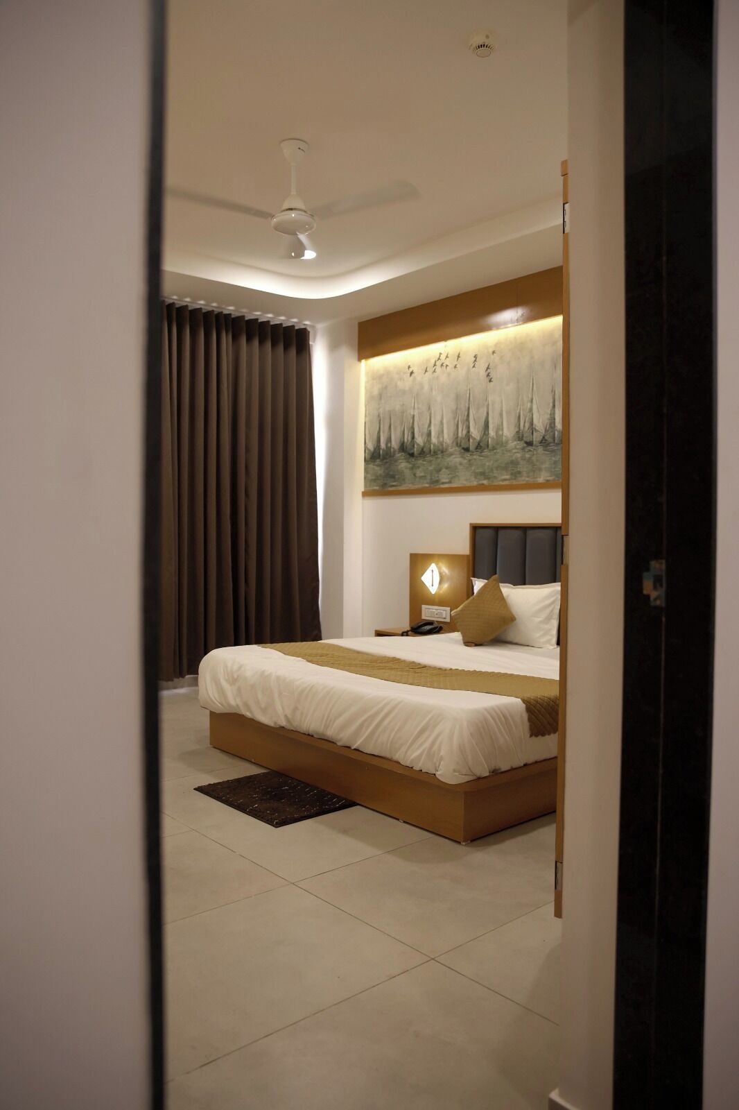 Een moderne slaapkamer met een groot bed, een plafondventilator, een schilderij en een nachtkastje.