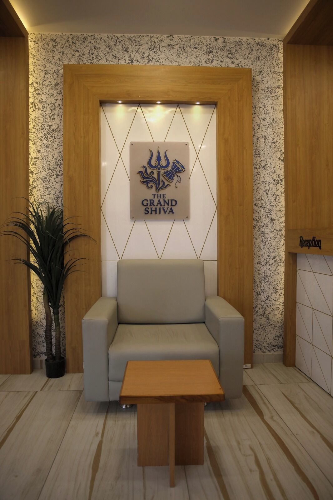 A reception area with a sofa, a wooden table, and a wall-mounted sign reading "The Grand Shiva".