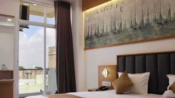 Une chambre d’hôtel avec un grand lit, un tableau représentant des voiliers, un ventilateur de plafond et une vue sur l’extérieur, visible à travers la porte vitrée.