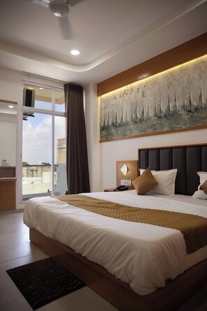 A hotel room with a large bed, a painting of sailboats, a ceiling fan, and a view through the glass door.