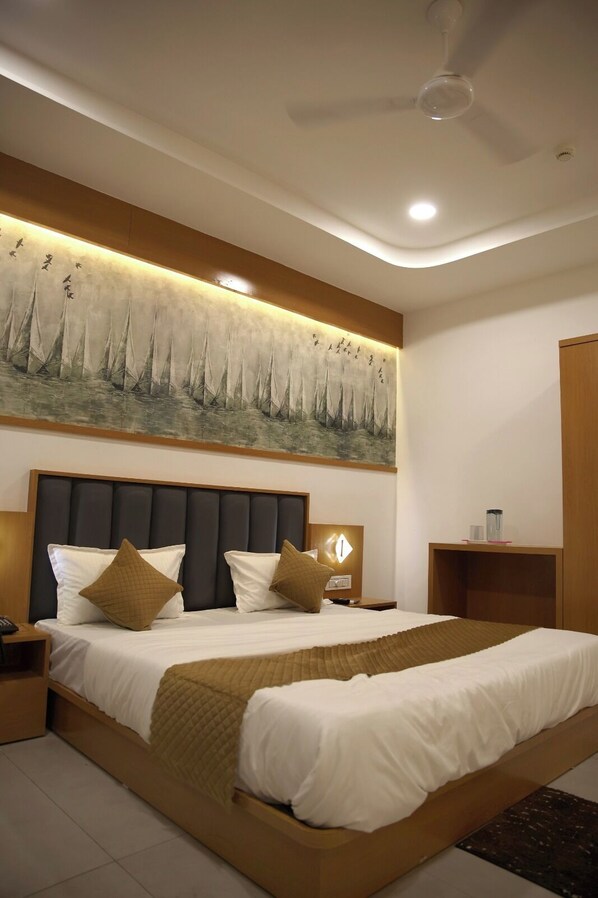 A modern hotel room with a large bed, a ceiling fan, a wall-mounted artwork, and a bedside table with a lamp.