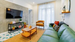 Una sala de estar moderna con un sofá verde, una mesa de centro de madera, un televisor montado en la pared y un ventanal con cortinas translúcidas.
