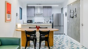 Cocina compacta con una isla central, dos sillas, una mesa de comedor y un refrigerador.