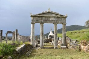 An ancient Greek temple with columns and a central structure, surrounded by ruins and a grassy landscape.