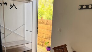 A room with a wooden dining table, a metal wardrobe, and a sliding glass door leading to an outdoor area with a wooden fence and a potted plant.