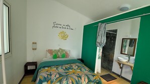 A bedroom with a bed, a green accent wall, a bathroom with a sink and mirror, and a decorative wall piece.