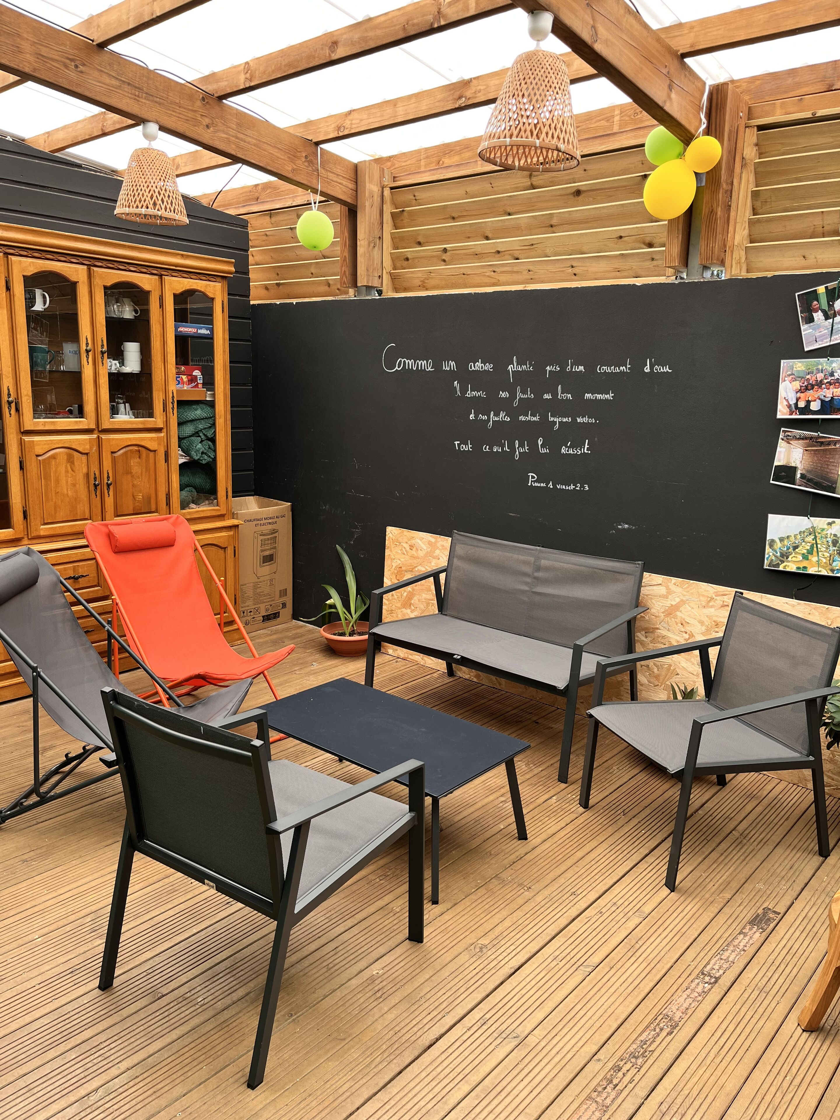 A wooden deck with outdoor furniture, a chalkboard with text, and a cabinet with glass doors.