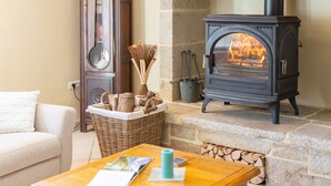 Un cuarto acogedor con chimenea, un sofá, una mesa de madera con revistas y una cesta de mimbre con leña.