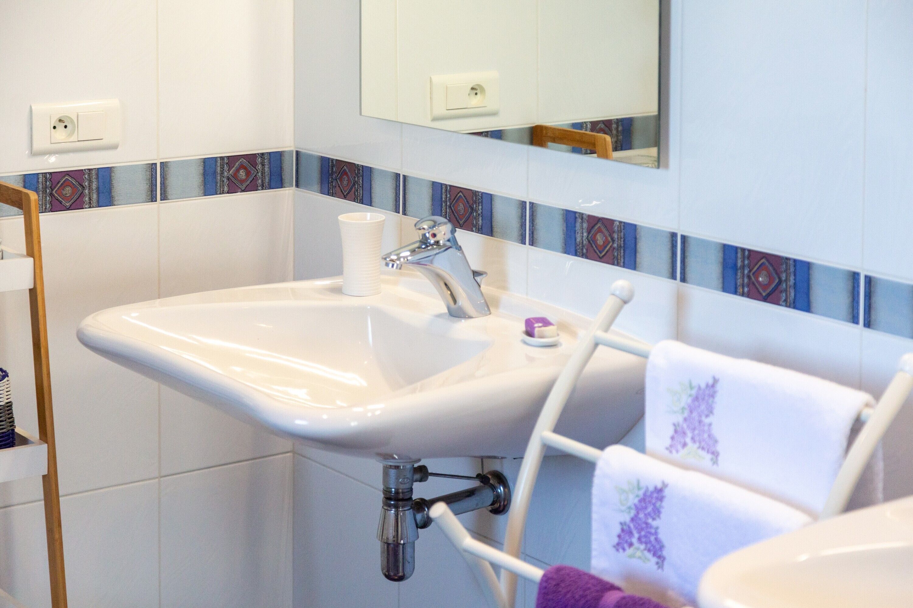 Ein Badezimmer mit einem weißen Waschbecken, einem Spiegel darüber und einer Fliesenküchenzeile mit Muster.