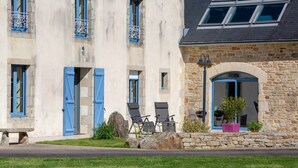 Un edificio de piedra con contraventanas azules, un banco de piedra y mesas al aire libre.